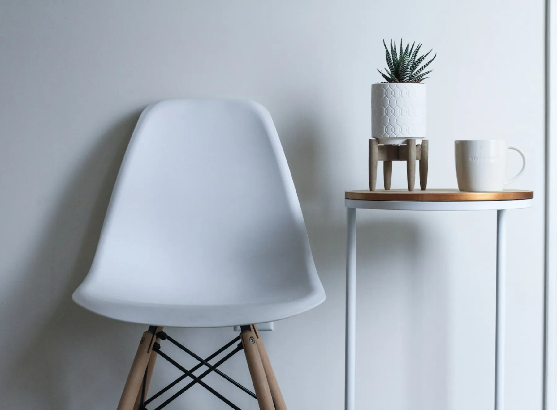 A calm still-life of a chair beside a plant and a warm drink